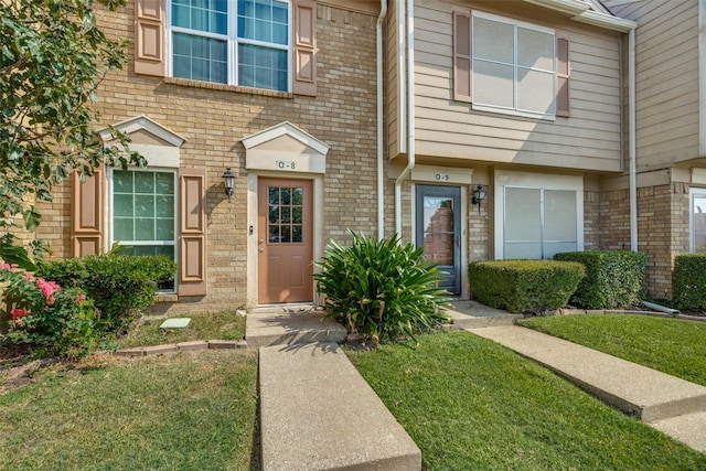 view of exterior entry featuring a yard and brick siding