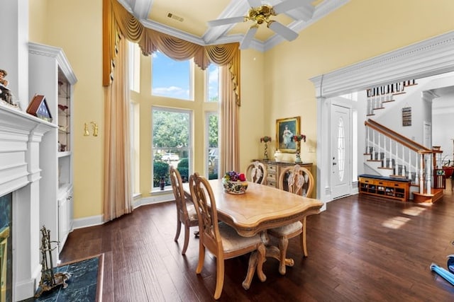 dining space featuring dark wood-type flooring, a towering ceiling, ceiling fan, crown molding, and a high end fireplace