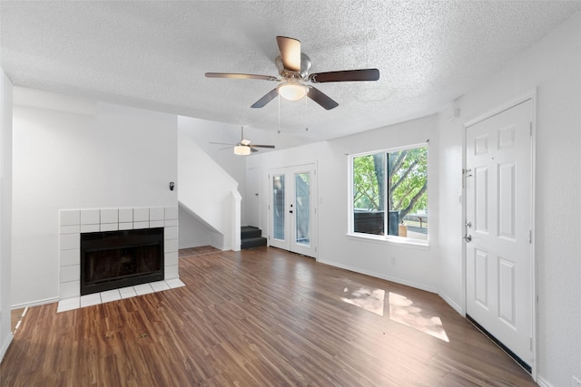 unfurnished living room with ceiling fan, a tile fireplace, a textured ceiling, french doors, and dark hardwood / wood-style flooring