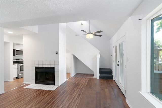 unfurnished living room with ceiling fan, vaulted ceiling, wood-type flooring, a tiled fireplace, and a textured ceiling