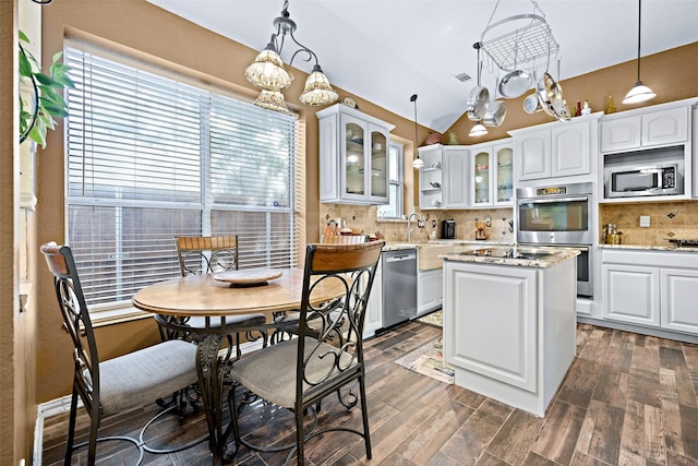 kitchen featuring light stone counters, a center island, pendant lighting, stainless steel appliances, and glass insert cabinets