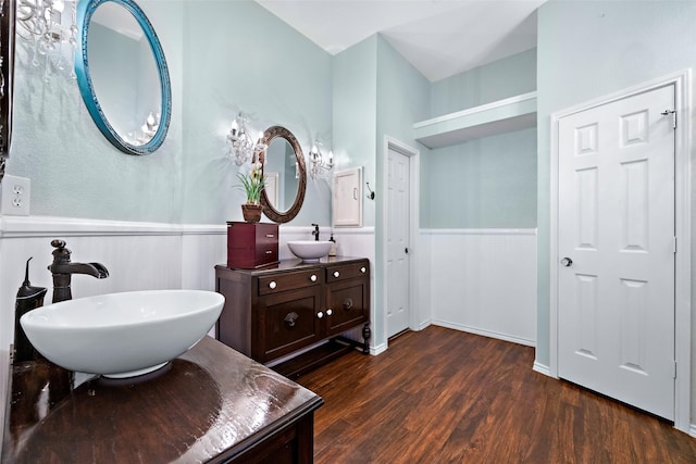 bathroom featuring wood finished floors, two vanities, a sink, and wainscoting