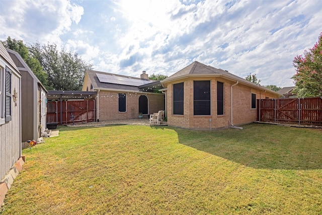 back of house featuring a fenced backyard, a chimney, a gate, a yard, and brick siding