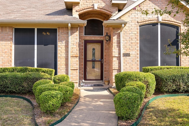 view of exterior entry featuring a shingled roof and brick siding