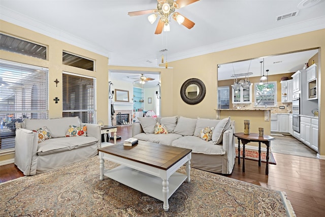 living area with visible vents, crown molding, a fireplace, and wood finished floors