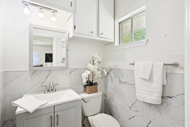 bathroom with a wainscoted wall, vanity, toilet, and tile walls