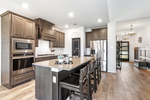 kitchen featuring light stone counters, custom exhaust hood, visible vents, appliances with stainless steel finishes, and light wood-type flooring