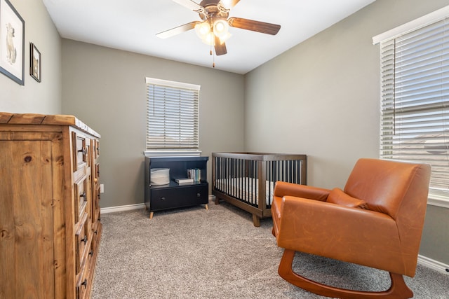 bedroom with carpet floors, a nursery area, baseboards, and a ceiling fan