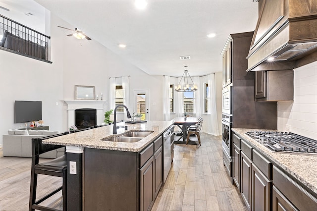 kitchen featuring light wood-type flooring, custom exhaust hood, stainless steel appliances, a kitchen island with sink, and sink