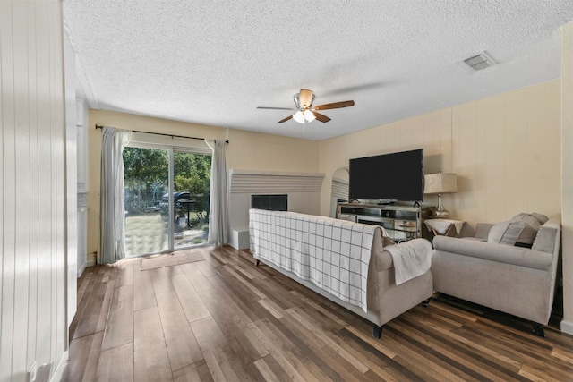 living room featuring ceiling fan, wood-type flooring, a textured ceiling, and a fireplace