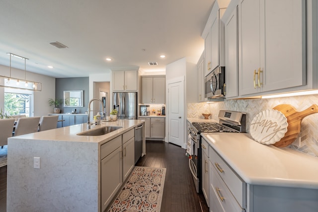 kitchen featuring decorative backsplash, pendant lighting, a kitchen island with sink, sink, and stainless steel appliances