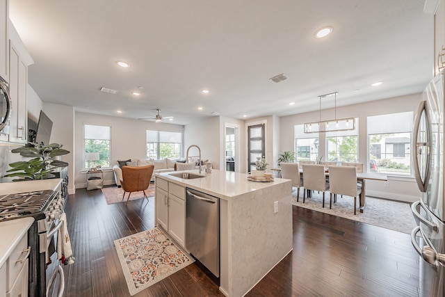 kitchen with dark hardwood / wood-style floors, ceiling fan, stainless steel appliances, pendant lighting, and a center island with sink