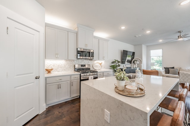 kitchen with dark wood-type flooring, decorative backsplash, a kitchen island, ceiling fan, and stainless steel appliances