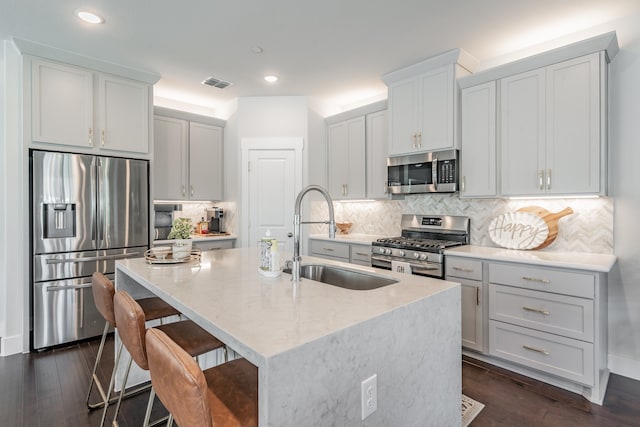 kitchen featuring backsplash, dark wood-type flooring, an island with sink, light stone counters, and stainless steel appliances