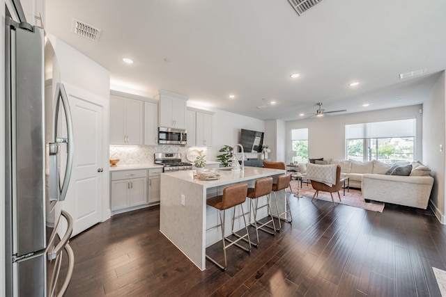 kitchen featuring dark hardwood / wood-style flooring, white cabinetry, appliances with stainless steel finishes, an island with sink, and ceiling fan