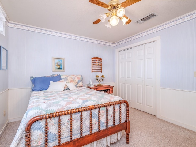 bedroom with a closet, light colored carpet, a wainscoted wall, and visible vents