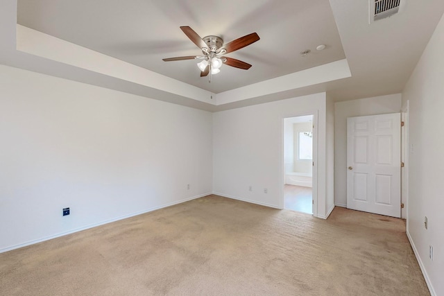 carpeted spare room with ceiling fan and a tray ceiling