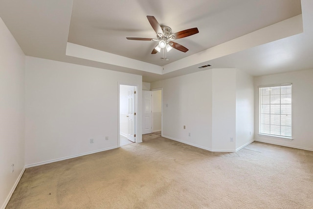 carpeted empty room featuring ceiling fan and a raised ceiling