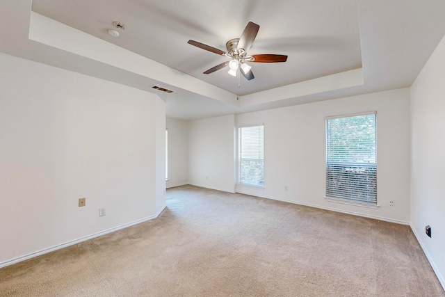 carpeted spare room with ceiling fan and a raised ceiling