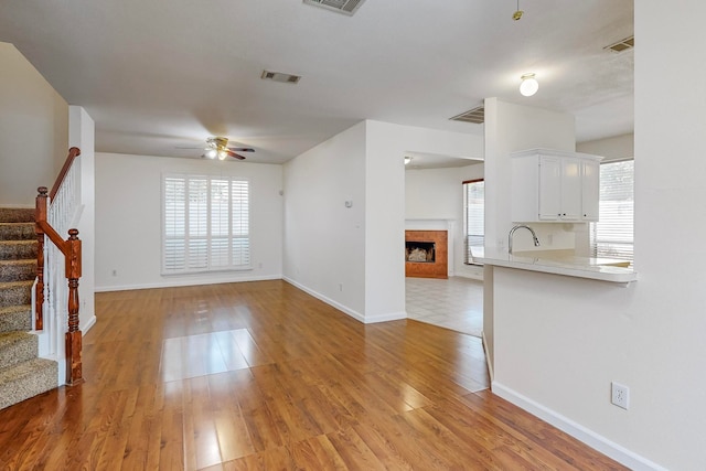 unfurnished living room featuring light hardwood / wood-style floors, a wealth of natural light, sink, and ceiling fan