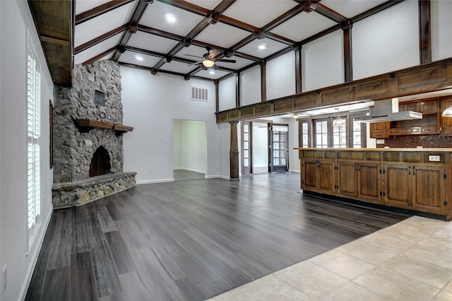 unfurnished living room with beam ceiling, hardwood / wood-style floors, a fireplace, ceiling fan, and a towering ceiling