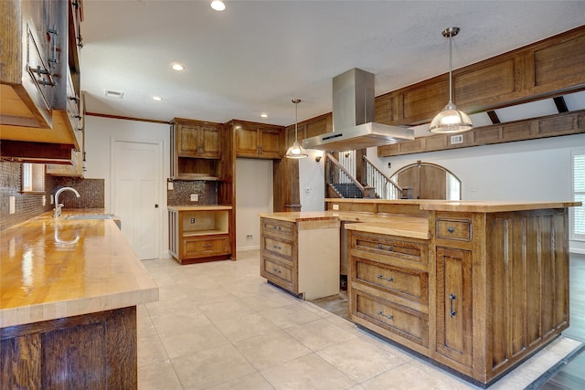 kitchen with sink, butcher block counters, tasteful backsplash, pendant lighting, and island range hood