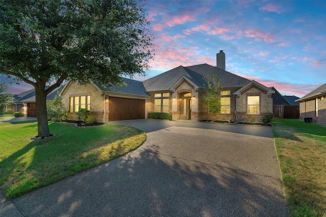 view of front of property with a garage, a yard, stone siding, driveway, and a chimney