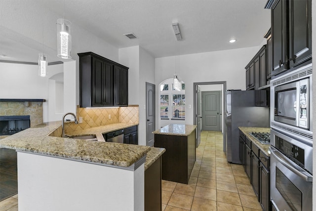 kitchen with sink, a center island, a fireplace, appliances with stainless steel finishes, and kitchen peninsula