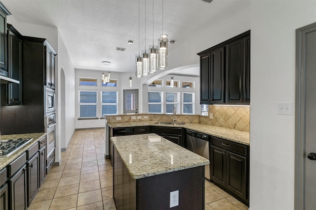 kitchen with backsplash, sink, light stone countertops, pendant lighting, and a center island