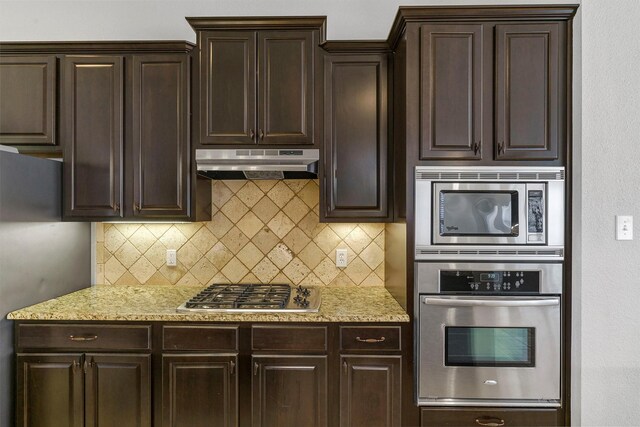 kitchen with appliances with stainless steel finishes, light stone countertops, dark brown cabinetry, and backsplash