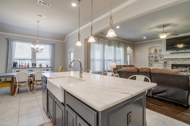 kitchen with light stone counters, light tile patterned floors, a fireplace, decorative light fixtures, and a center island with sink