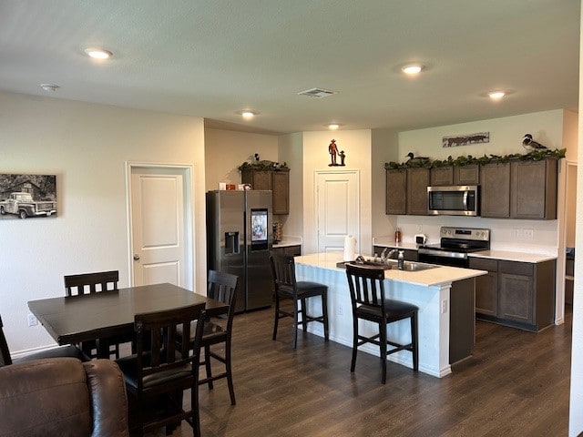 kitchen featuring a kitchen island with sink, a kitchen bar, sink, dark wood-type flooring, and appliances with stainless steel finishes