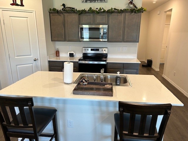 kitchen with a center island with sink, stainless steel appliances, sink, and dark hardwood / wood-style flooring