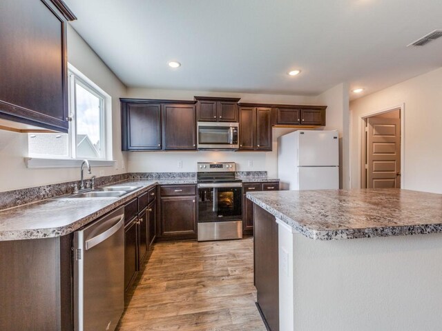 kitchen with a center island, stainless steel appliances, sink, wood-type flooring, and dark brown cabinetry