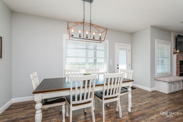 dining area featuring dark wood-style floors, a brick fireplace, a chandelier, and baseboards