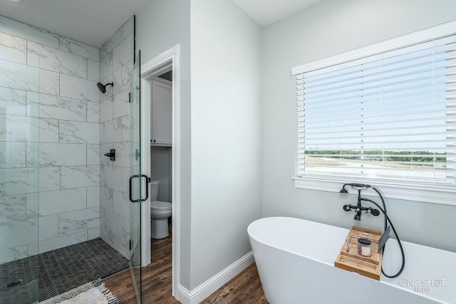 bathroom with toilet, wood finished floors, baseboards, a freestanding bath, and a stall shower