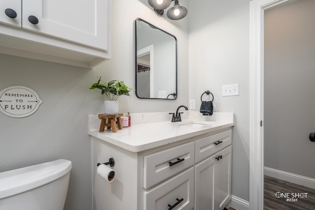 half bathroom with toilet, baseboards, wood finished floors, and vanity