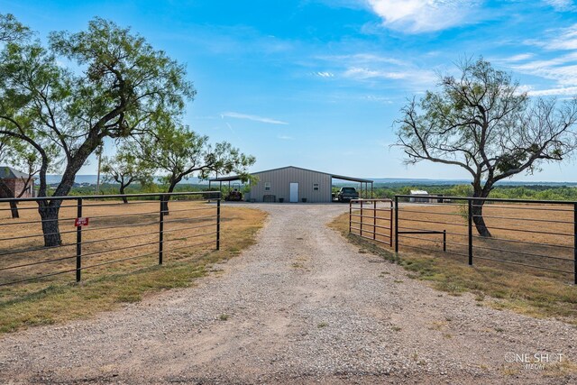 view of street featuring a pole building, a rural view, gravel driveway, and a gated entry