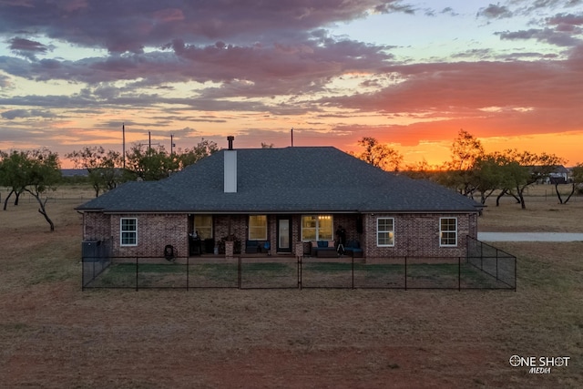 back of house at dusk with a fenced front yard, brick siding, and a shingled roof