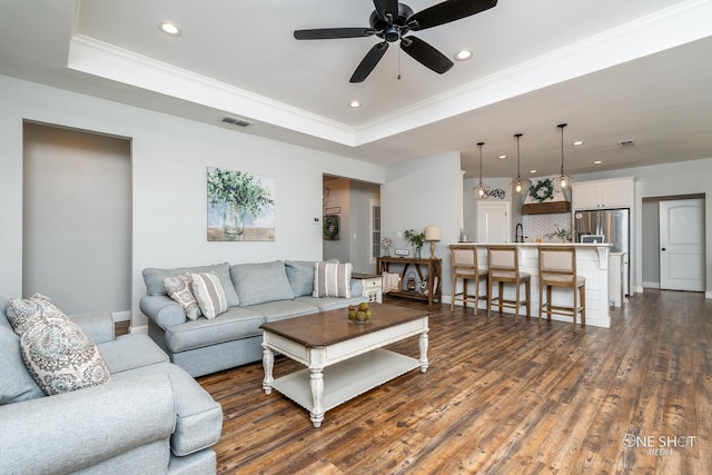 living room with visible vents, dark wood-style flooring, a tray ceiling, crown molding, and recessed lighting