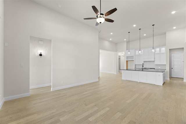 kitchen with ceiling fan, decorative light fixtures, light hardwood / wood-style flooring, white cabinetry, and an island with sink