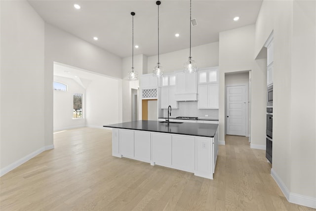 kitchen featuring white cabinets, a center island with sink, sink, decorative backsplash, and decorative light fixtures