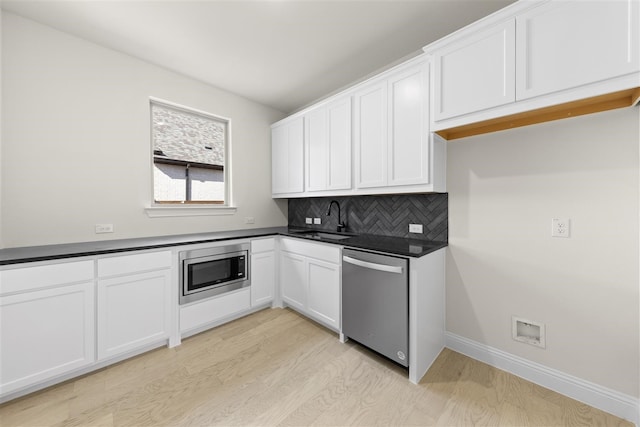 kitchen featuring sink, decorative backsplash, appliances with stainless steel finishes, light hardwood / wood-style floors, and white cabinetry