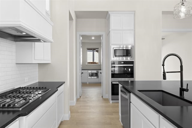 kitchen with premium range hood, white cabinets, sink, hanging light fixtures, and stainless steel appliances