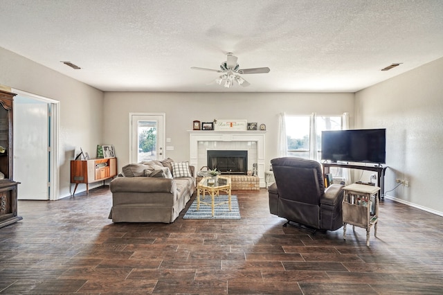 living room featuring ceiling fan, a textured ceiling, and a fireplace