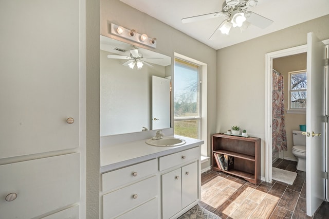 bathroom with ceiling fan, toilet, vanity, and a wealth of natural light