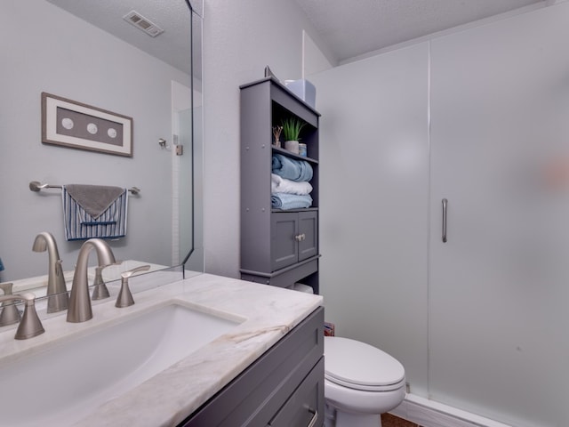 bathroom with a textured ceiling, a shower with door, toilet, and vanity