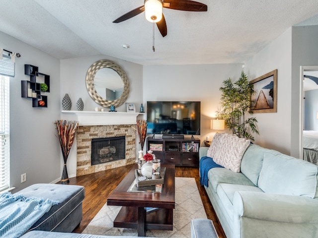 living room featuring hardwood / wood-style floors, a stone fireplace, ceiling fan, and a textured ceiling