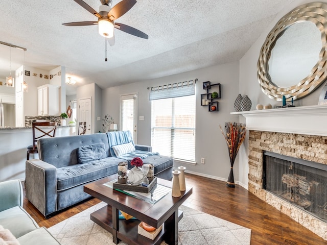 living room with a textured ceiling, ceiling fan, hardwood / wood-style floors, and a stone fireplace