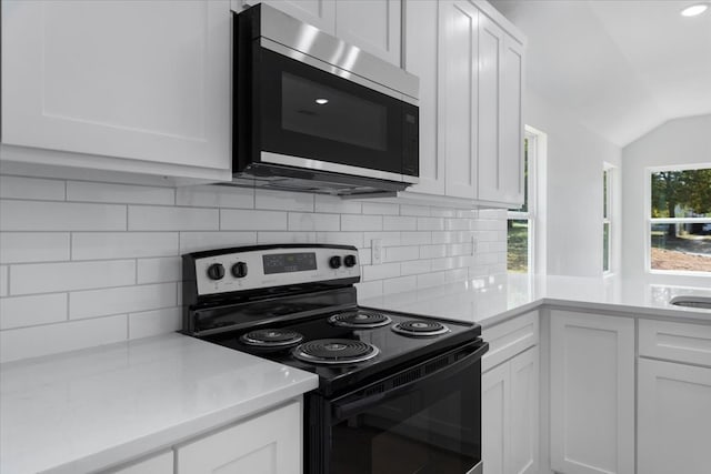 kitchen featuring appliances with stainless steel finishes, vaulted ceiling, decorative backsplash, and white cabinets